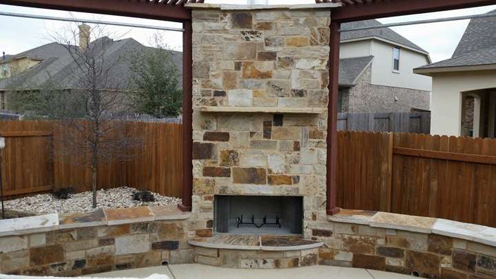 Outdoor stone fireplace with a pergola surround and curved limestone seating walls