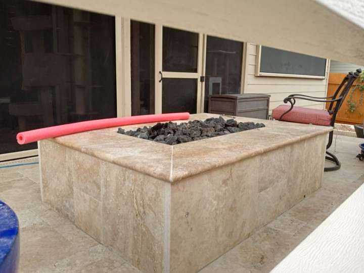 Rectangular travertine fire pit with lava rock on a patio
