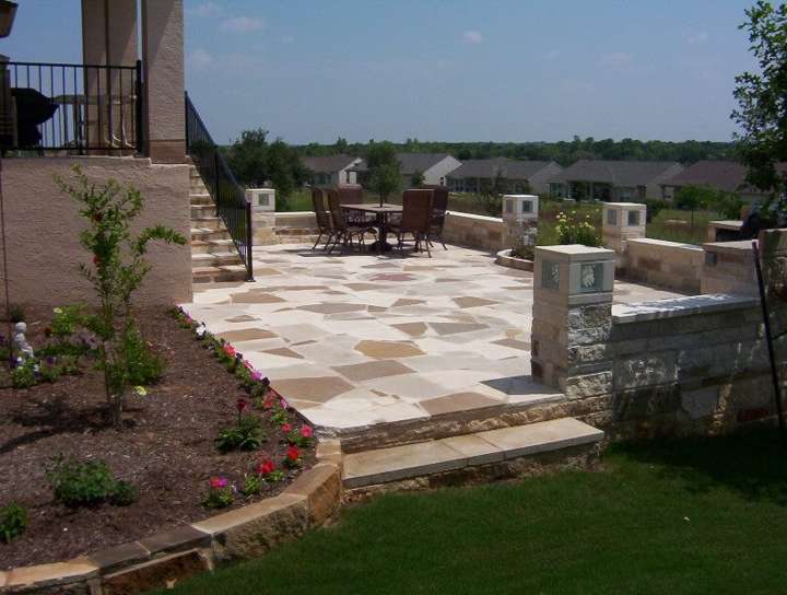 Flagstone patio with limestone columns, a dining set and planted beds
