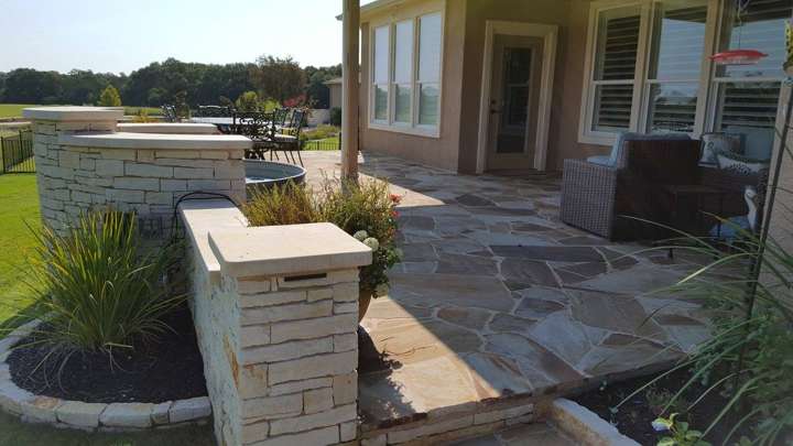 Flagstone patio and limestone column beside a covered porch with seating