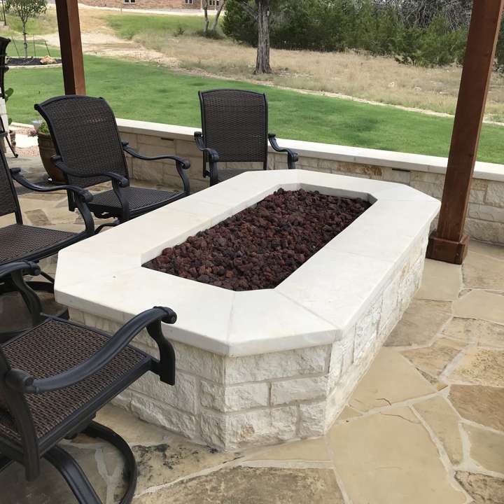 Rectangular limestone fire pit with lava rock on a flagstone patio under a pergola