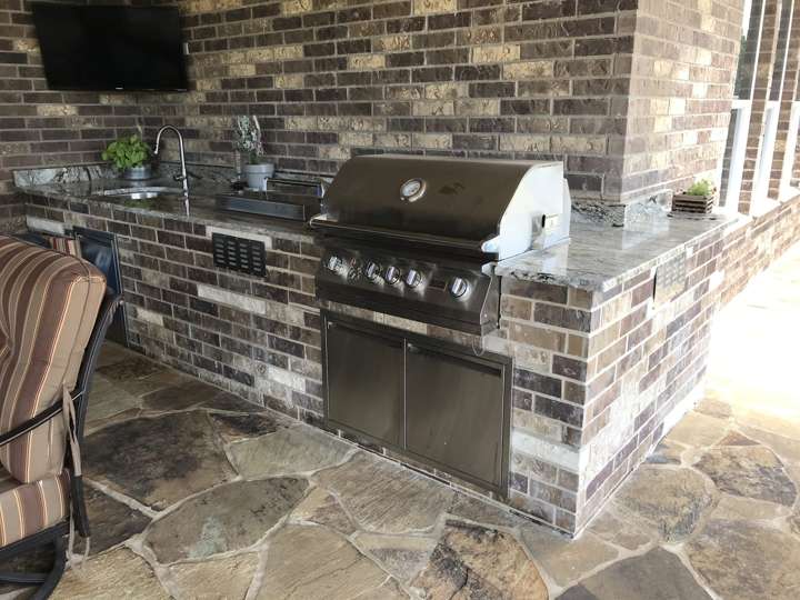 Outdoor kitchen in dark mixed stone with a built-in grill under a porch