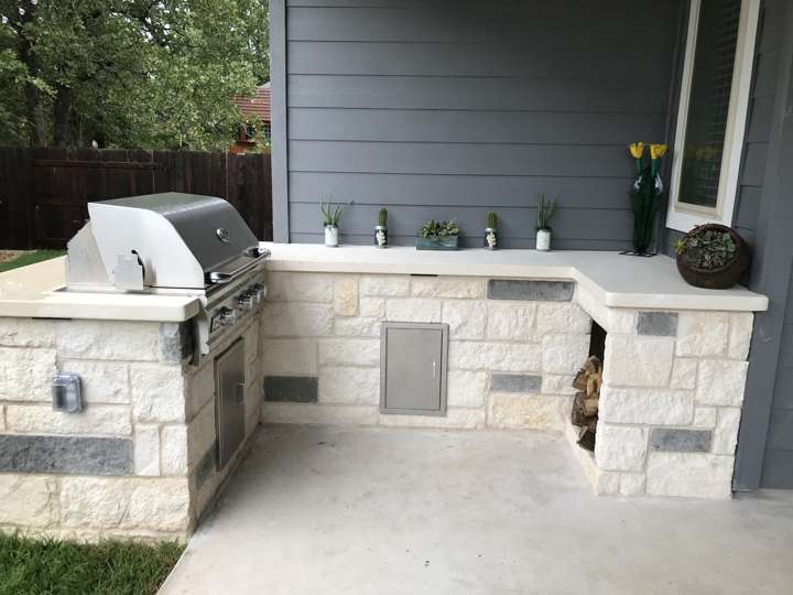 L-shaped limestone outdoor kitchen with built-in grill and storage on a covered patio