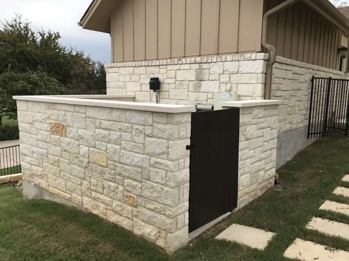 Chopped limestone equipment enclosure with a gate beside a house