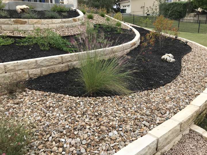 Curved chopped-limestone edging holding a mulched native bed against a lawn