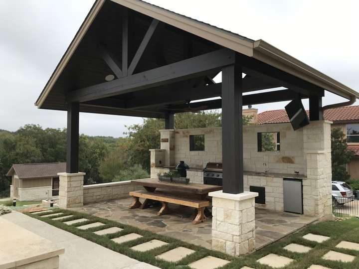 Covered outdoor kitchen with a gabled roof, picnic table and stone island