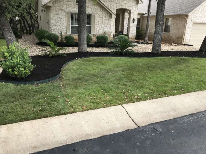 Front yard beds with black mulch and limestone edging under mature trees