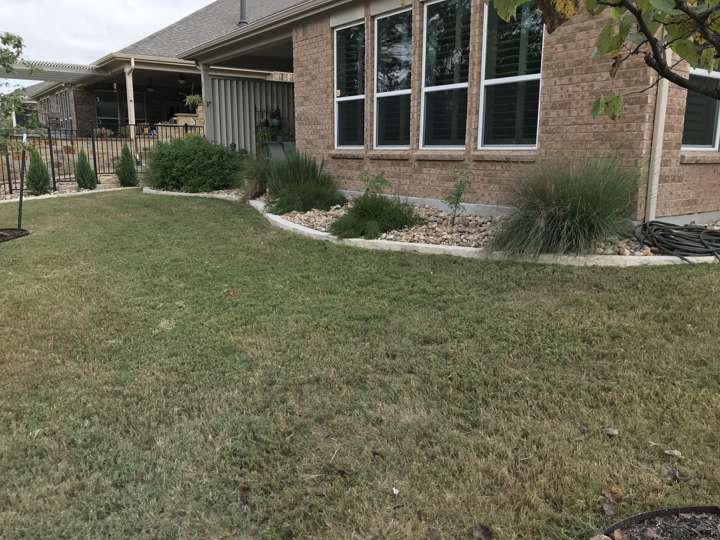Back yard with a mulched bed and iron fence beyond a covered porch