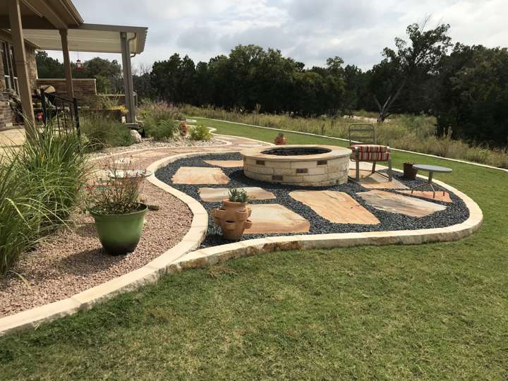 Stone fire pit on a flagstone pad with gravel and limestone-edged beds in a back yard