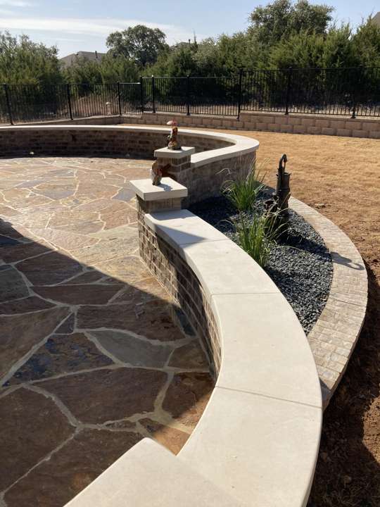Curved limestone seat wall around a flagstone patio on a large lot