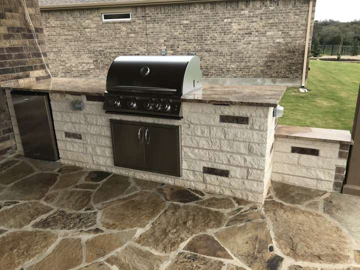 Chopped limestone outdoor kitchen with grill and access door on a flagstone patio