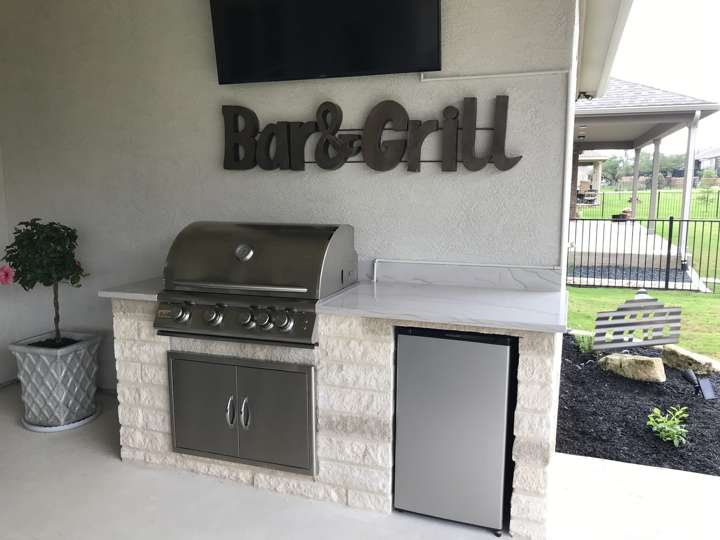 Outdoor grill station in white stone with a bar-and-grill sign above