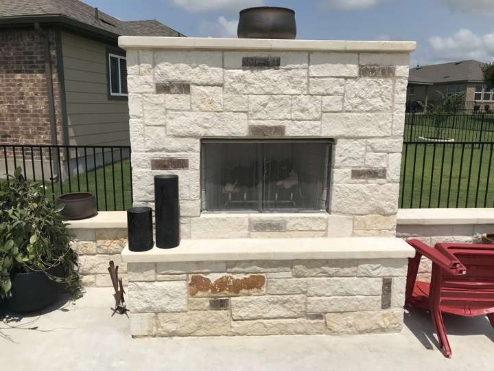 Chopped limestone outdoor fireplace with a TV above and seating on a patio