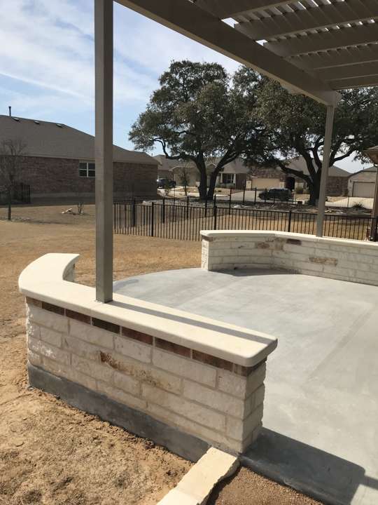 Limestone seat wall and concrete pad under a pergola