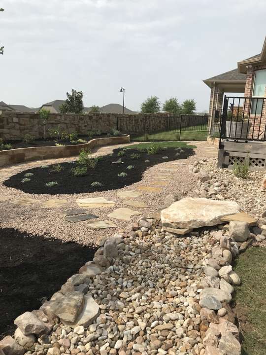 River-rock dry creek bed through a gravel yard beside a house