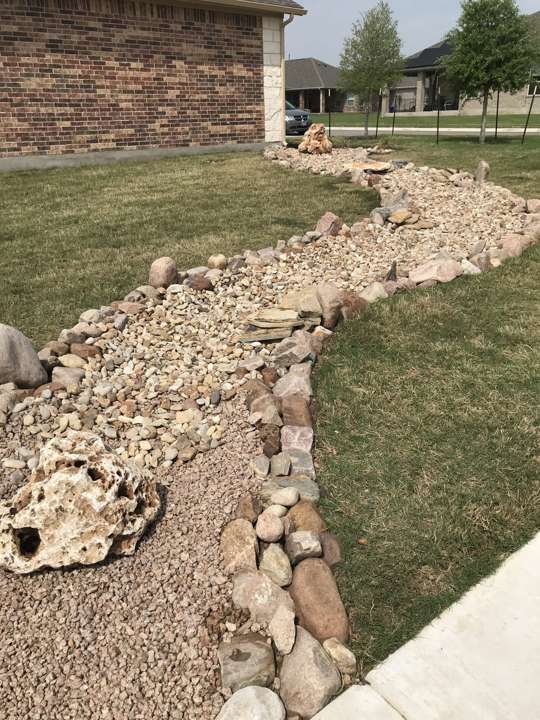 Dry creek bed of river rock with limestone boulders along a lawn edge