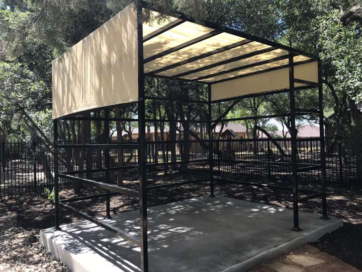 Steel shade structure over a concrete pad under live oaks