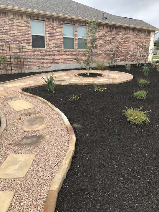 Decomposed granite path curving through black mulch beds beside a house