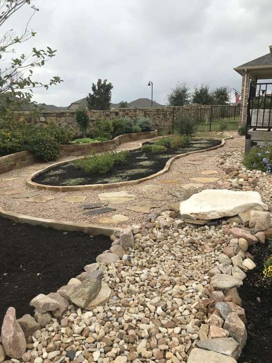 Dry creek bed of river rock running to a lawn with steppers
