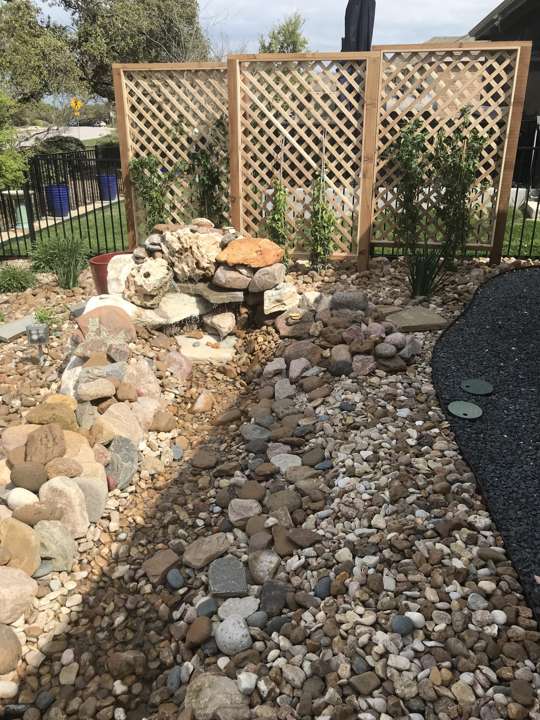 Boulder fountain in a river-rock bed beside a lattice screen