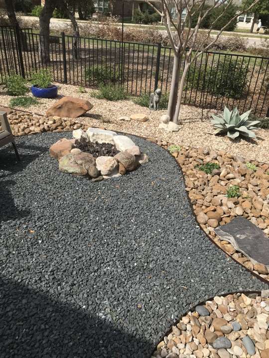 Stone fire pit set in a gravel bed with native plants and an iron fence