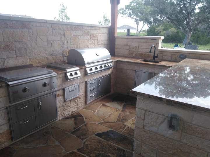 Outdoor kitchen with granite counter, grill and sink under a covered patio