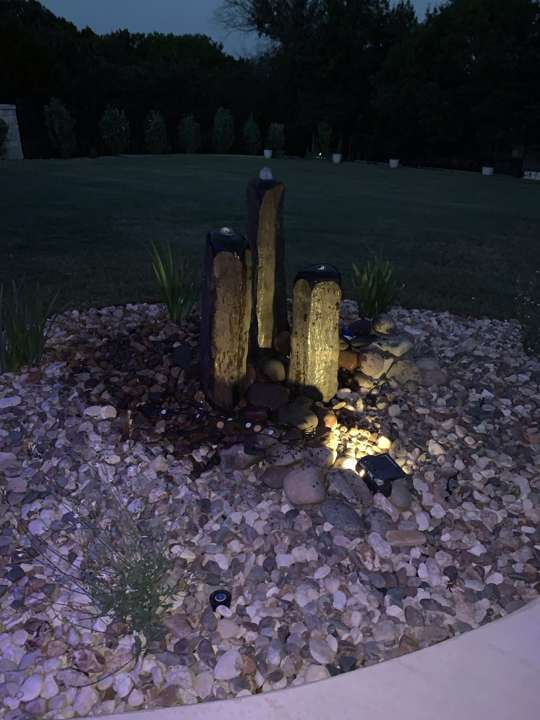 Lit stone column fountain in a gravel bed at night