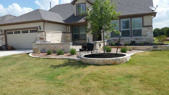 New-construction front yard with a raised chopped-limestone planter and a young shade tree