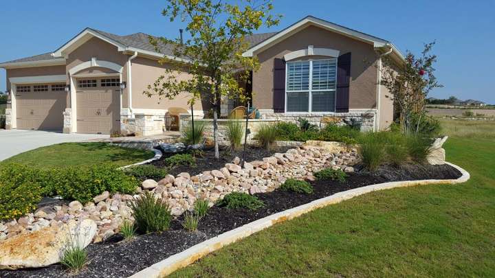 River-rock bed with limestone edging and native plants along a front walk
