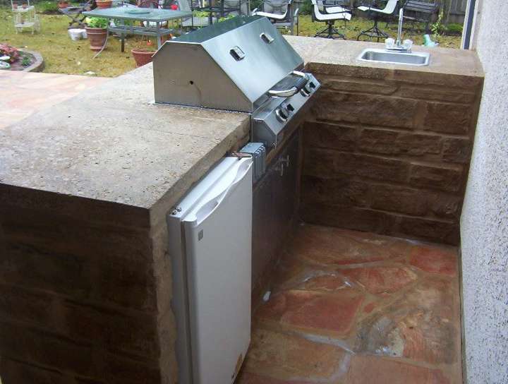 Sandstone outdoor kitchen with a raised bar, grill and refrigerator
