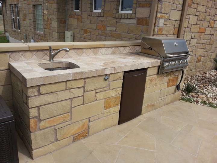 Outdoor kitchen built from Texas stone with a travertine countertop, sink and built-in grill