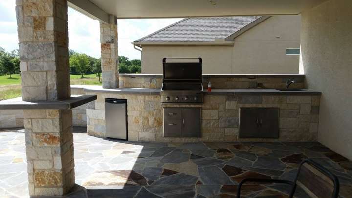 Covered outdoor kitchen in chopped stone on a flagstone patio