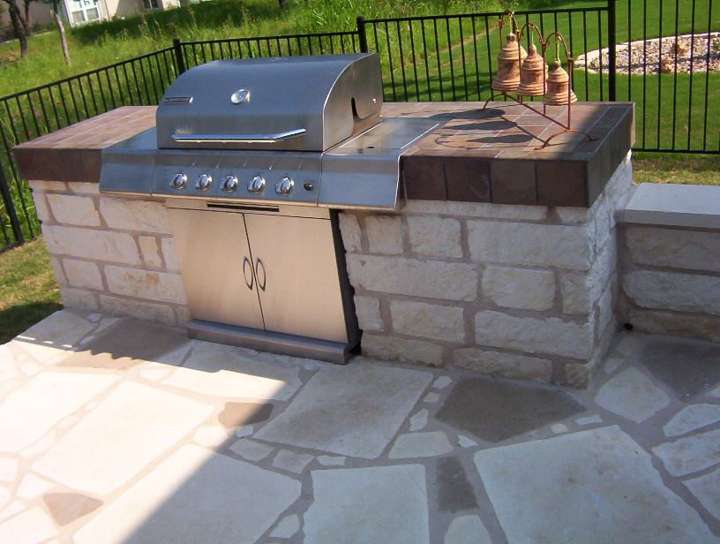 Built-in grill in a limestone counter with a dark stone top on flagstone