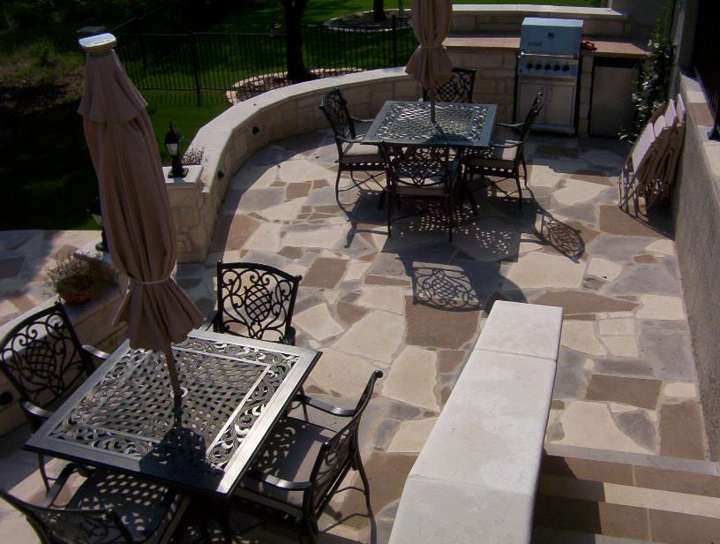 Flagstone patio with a curved limestone seat wall, dining set and built-in grill under a covered porch