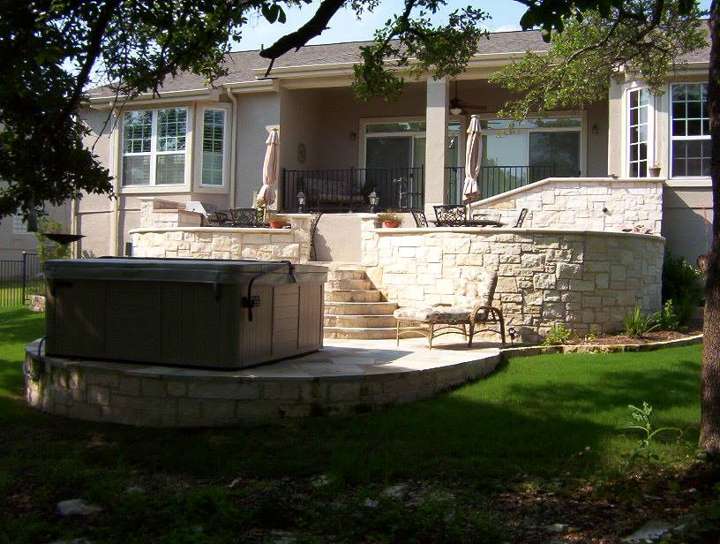 Raised limestone patio with seat walls, a hot tub and steps down to the lawn