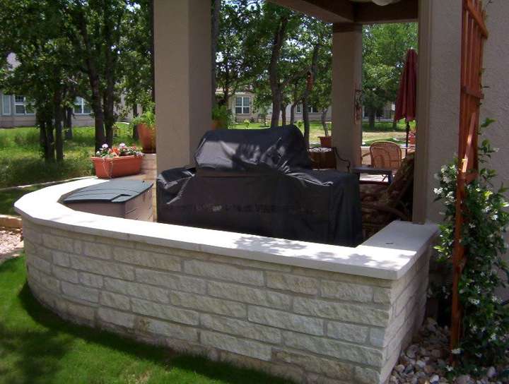 Curved limestone seat wall with a grill and umbrella on a patio