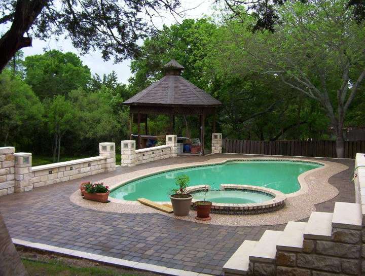 Pool deck in pavers with a limestone coping wall and a gazebo beyond