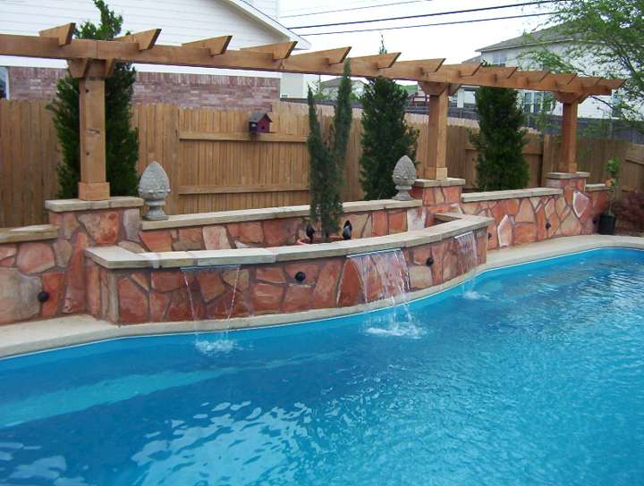 Stone spillway wall with pergola posts along a pool