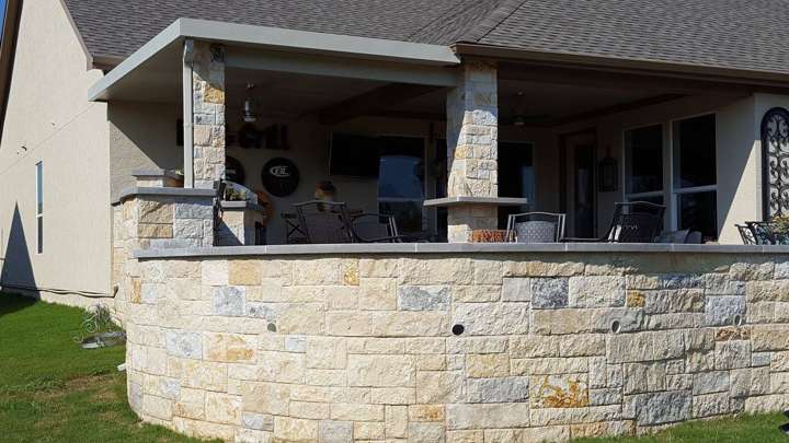 Covered outdoor kitchen and bar in chopped Texas limestone with a curved seat wall