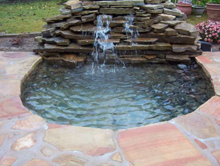 Stacked-stone waterfall into a round basin beside a flagstone patio