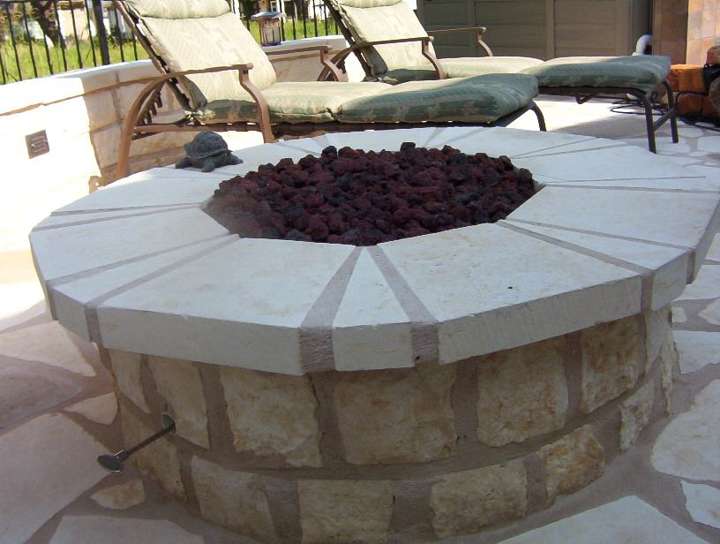Round limestone gas fire pit with lava rock on a pool deck