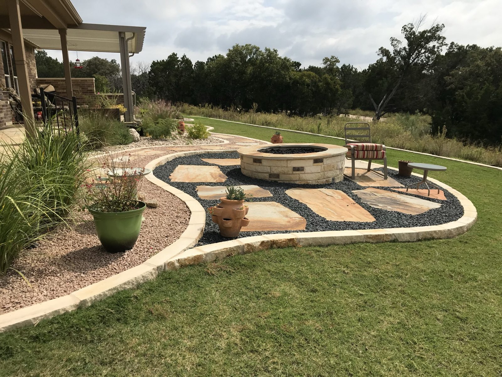 Flagstone patio with a stone fire pit and limestone-edged beds stepping down a sloped back yard, a B&B project in Williamson County, Texas