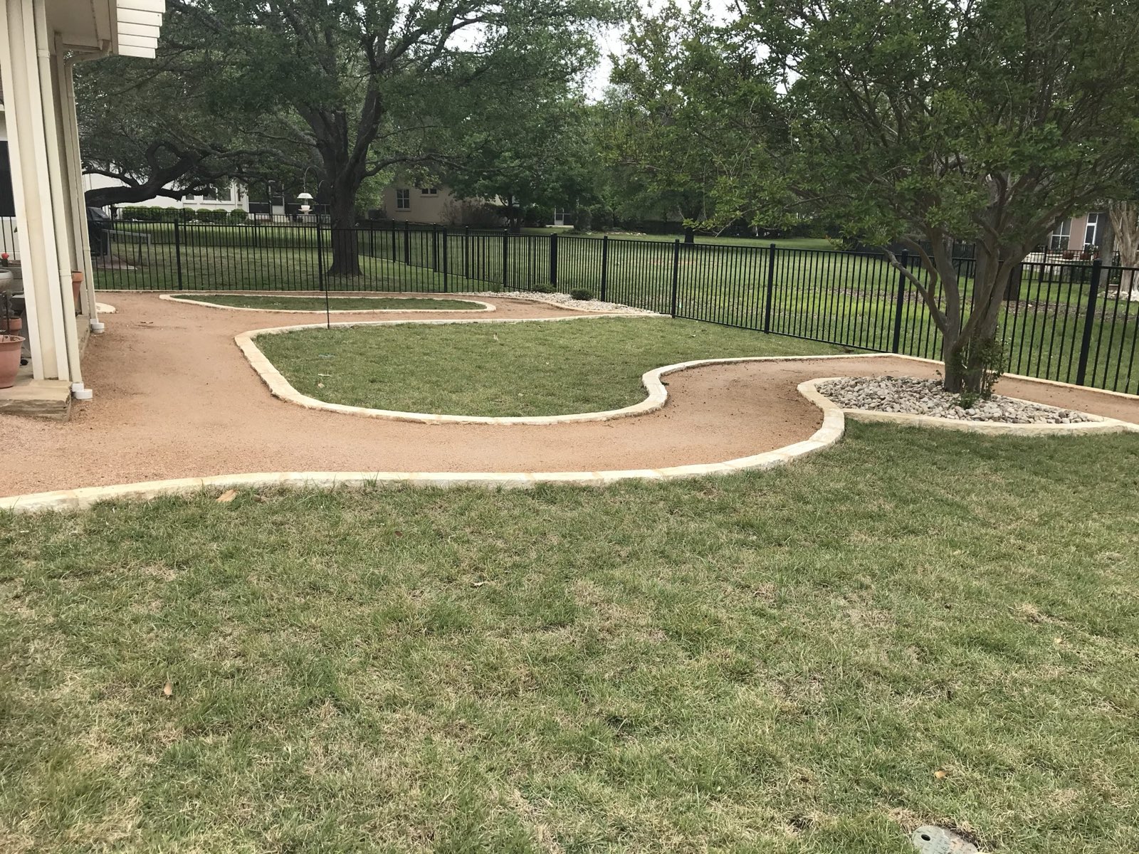 Decomposed-granite path with limestone edging crossing a large lawn under mature trees to an iron fence, a B&B project in Williamson County, Texas