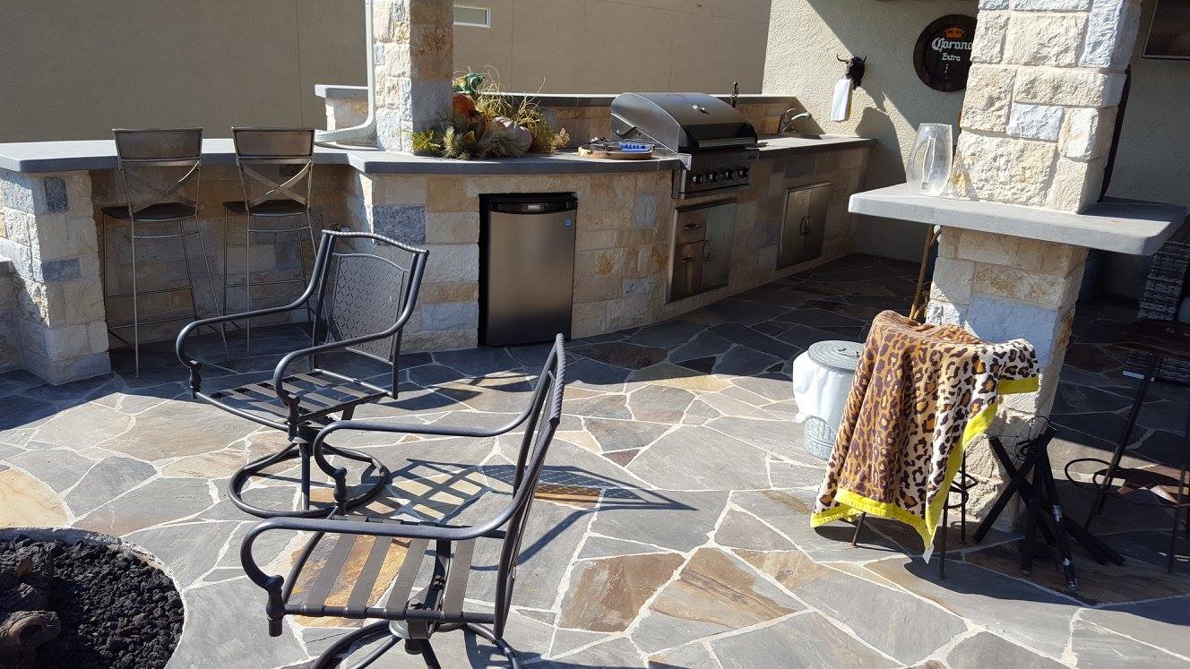 Flagstone patio with a built-in stone outdoor kitchen, bar seating and fire pit built by B&B in Georgetown, Texas