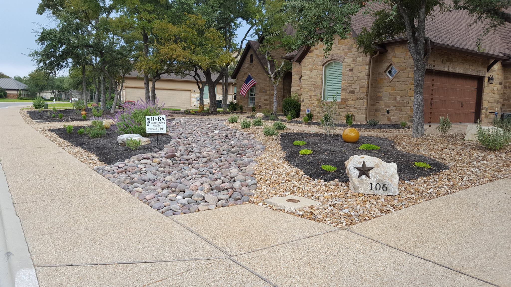 Xeriscaped front yard in Georgetown, Texas with a river-rock dry creek bed, limestone address boulder and native planting